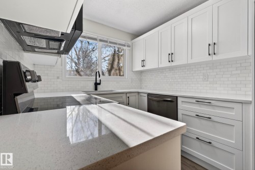 Kitchen featuring white cabinetry, range hood, light stone counters, backsplash, and a textured ceiling - 9969 171 Avenue, Edmonton, AB - Indoor Photo Showing Other Room