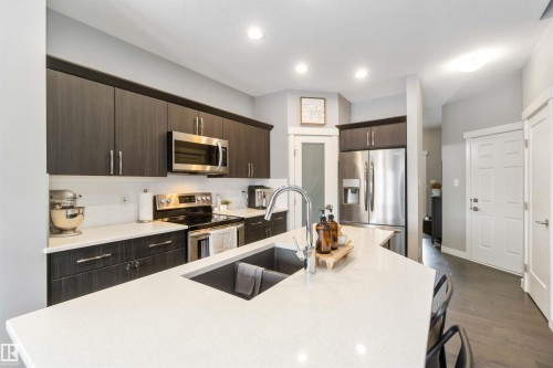 Kitchen featuring dark wood finish cabinets, a center island with sink, stainless steel appliances, dark wood-style floors, and light stone counters - 17143 38 Street, Edmonton, AB - Indoor Photo Showing Kitchen With Upgraded Kitchen