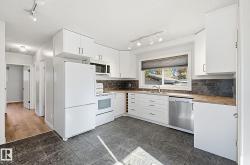 Kitchen with track lighting, white appliances, white cabinetry, wood counters, and tasteful backsplash - 12107 53 Street, Edmonton, AB - Indoor Photo Showing Kitchen With Double Sink