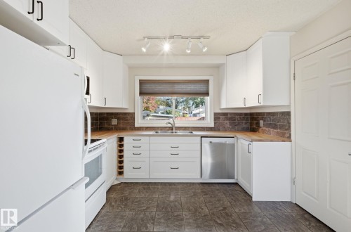 Kitchen featuring white appliances, white cabinetry, butcher block countertops, tasteful backsplash, and a textured ceiling - 12107 53 Street, Edmonton, AB - Indoor Photo Showing Kitchen With Double Sink