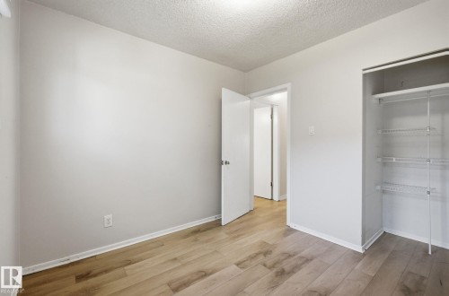Unfurnished bedroom with light wood-type flooring, a textured ceiling, and a closet - 12107 53 Street, Edmonton, AB - Indoor Photo Showing Other Room