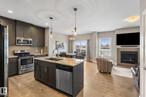 Kitchen featuring stainless steel appliances, light stone countertops, light wood finished floors, tasteful backsplash, and a textured ceiling - 1043 South Creek Wynd, Stony Plain, AB - Indoor Photo Showing Kitchen With Fireplace With Double Sink With Upgraded Kitchen
