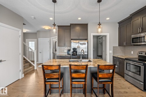 Kitchen featuring stainless steel appliances, light stone counters, dark wood finish cabinets, a kitchen island with sink, and a textured ceiling - 1043 South Creek Wynd, Stony Plain, AB - Indoor Photo Showing Kitchen With Double Sink With Upgraded Kitchen