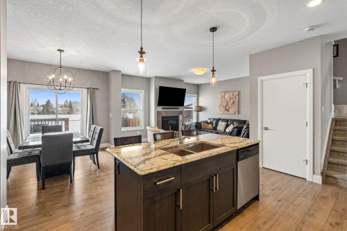 Kitchen with light stone countertops, light wood finished floors, open floor plan, a kitchen island with sink, and dark wood finish cabinetry - 1043 South Creek Wynd, Stony Plain, AB - Indoor Photo Showing Other Room