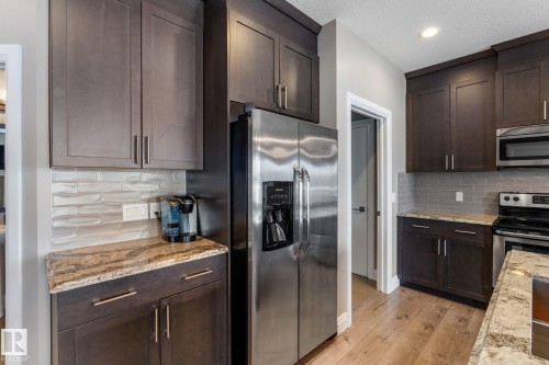 Kitchen featuring dark wood finish cabinetry, stainless steel appliances, light stone countertops, recessed lighting, and light wood-style flooring - 1043 South Creek Wynd, Stony Plain, AB - Indoor Photo Showing Kitchen