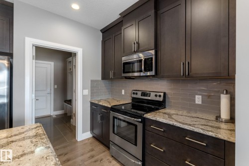 Kitchen with stainless steel appliances, dark wood finish cabinets, light stone countertops, tasteful backsplash, and recessed lighting - 1043 South Creek Wynd, Stony Plain, AB - Indoor Photo Showing Kitchen With Upgraded Kitchen