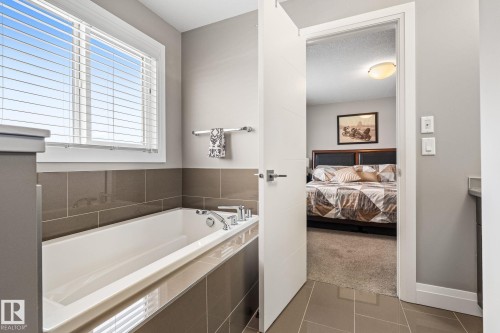 Bathroom featuring connected bathroom, light carpet, a bath, light tile patterned floors, and vanity - 1043 South Creek Wynd, Stony Plain, AB - Indoor Photo Showing Bathroom