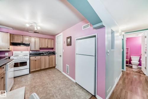 Kitchen featuring white appliances, dark countertops, and light wood finish cabinetry - 9823 75 Avenue, Edmonton, AB - Indoor Photo Showing Kitchen With Double Sink