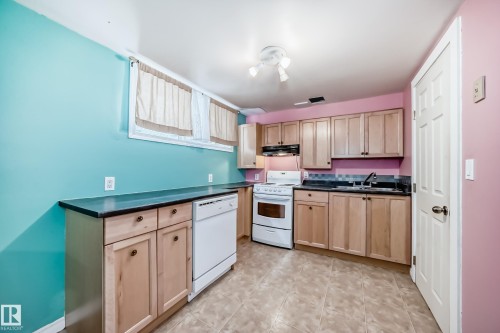 Kitchen with white appliances, light wood finish cabinetry, dark countertops, and light tile patterned floors - 9823 75 Avenue, Edmonton, AB - Indoor Photo Showing Kitchen With Double Sink