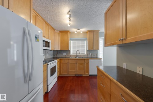 Kitchen with white appliances, dark countertops, decorative backsplash, dark wood-type flooring, and a textured ceiling - 9916 178 Avenue, Edmonton, AB - Indoor Photo Showing Kitchen With Double Sink