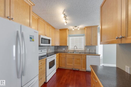 Kitchen featuring white appliances, dark countertops, light wood finish cabinetry, dark wood-style floors, and a textured ceiling - 9916 178 Avenue, Edmonton, AB - Indoor Photo Showing Kitchen With Double Sink