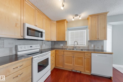 Kitchen with white appliances, light wood finish cabinets, decorative backsplash, dark wood finished floors, and a textured ceiling - 9916 178 Avenue, Edmonton, AB - Indoor Photo Showing Kitchen With Double Sink