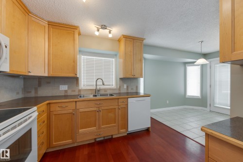Kitchen featuring white appliances, decorative backsplash, dark countertops, light wood finish cabinetry, and a textured ceiling - 9916 178 Avenue, Edmonton, AB - Indoor Photo Showing Kitchen With Double Sink