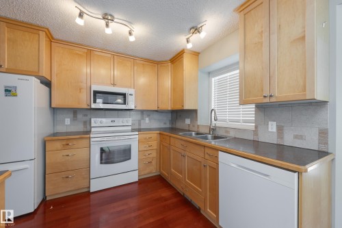 Kitchen featuring white appliances, a textured ceiling, decorative backsplash, dark wood-type flooring, and dark countertops - 9916 178 Avenue, Edmonton, AB - Indoor Photo Showing Kitchen With Double Sink