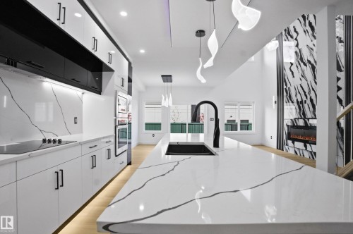 Kitchen featuring white cabinetry, hanging light fixtures, light wood-style floors, a large island with sink, and light stone counters - 15415 20 Street, Edmonton, AB - Indoor Photo Showing Kitchen With Upgraded Kitchen