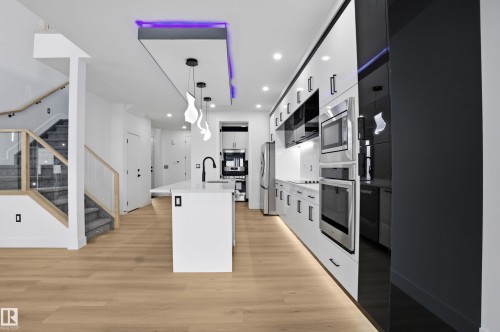 Kitchen with pendant lighting, modern cabinets, light wood-style flooring, a center island with sink, and white cabinetry - 15415 20 Street, Edmonton, AB - Indoor