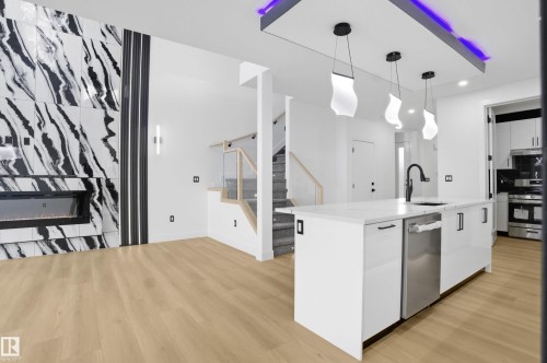Kitchen with decorative light fixtures, white cabinets, a kitchen island with sink, stainless steel appliances, and light wood-type flooring - 15415 20 Street, Edmonton, AB - Indoor Photo Showing Kitchen With Upgraded Kitchen