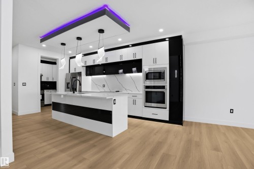 Kitchen with white cabinetry, a kitchen island with sink, pendant lighting, stainless steel appliances, and light wood-style floors - 15415 20 Street, Edmonton, AB - Indoor Photo Showing Kitchen
