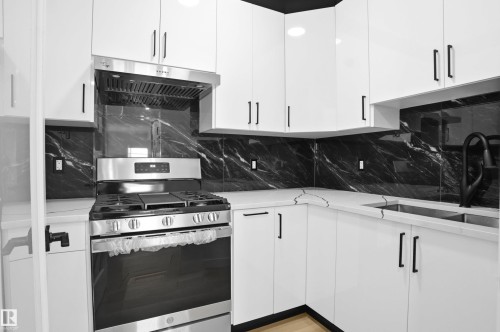 Kitchen with stainless steel gas range, white cabinetry, extractor fan, decorative backsplash, and light stone countertops - 15415 20 Street, Edmonton, AB - Indoor Photo Showing Kitchen With Upgraded Kitchen