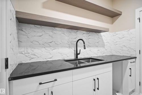 Kitchen with open shelves, white cabinetry, dark stone countertops, and tasteful backsplash - 3910 41 Avenue, Beaumont, AB - Indoor Photo Showing Kitchen With Double Sink
