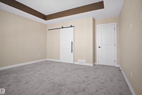 Unfurnished bedroom featuring a barn door, carpet flooring, and a tray ceiling - 3910 41 Avenue, Beaumont, AB - Indoor Photo Showing Other Room