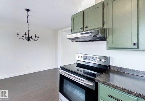 Kitchen with green cabinetry, electric range, extractor fan, a chandelier, and dark wood finished floors - 1102 55 Street, Edson, AB - Indoor Photo Showing Kitchen