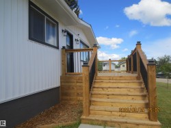 Expansive wood deck with black metal balusters and post caps, complemented by a white vertical siding exterior and dark window trim - 