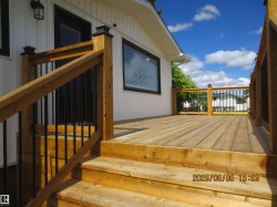Spacious wooden deck with natural finish, featuring black metal balusters, wooden railings, and post caps - 
