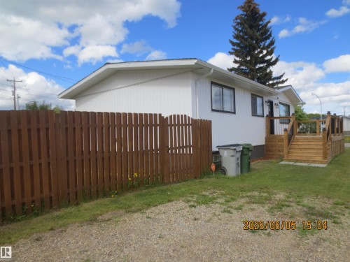 Property exterior featuring white siding, a brown wooden privacy fence, a wooden deck with dark railings, and a gravel and grass yard - 1102 55 Street, Edson, AB 