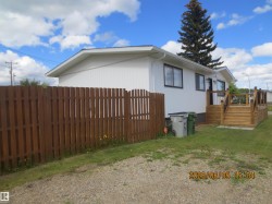 Property exterior featuring white siding, a brown wooden privacy fence, a wooden deck with dark railings, and a gravel and grass yard - 