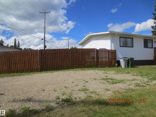Gravel driveway featuring a wood privacy fence and a white exterior home with dark window trim - 1102 55 Street, Edson, AB 