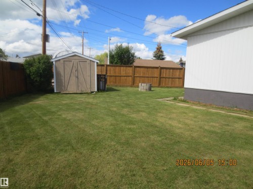 Expansive rear yard featuring a wooden privacy fence, a storage shed, and a concrete block fire pit - 1102 55 Street, Edson, AB 