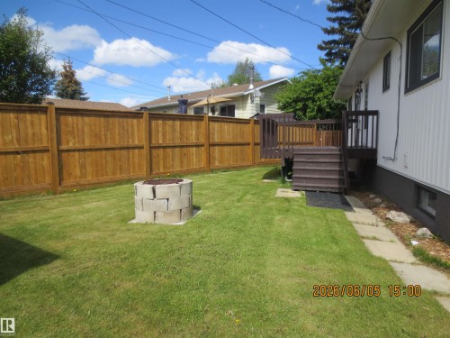 Expansive backyard featuring a stained wood privacy fence, a concrete block fire pit, a multi-level wood deck, a stone paver pathway, and a white siding exterior - 1102 55 Street, Edson, AB 