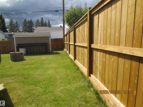 Expansive green lawn backyard featuring a new wood privacy fence, a detached shed with a brown shingle roof, and a stone-look fire pit - 1102 55 Street, Edson, AB 