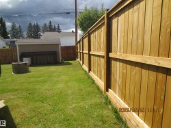 Expansive green lawn backyard featuring a new wood privacy fence, a detached shed with a brown shingle roof, and a stone-look fire pit - 