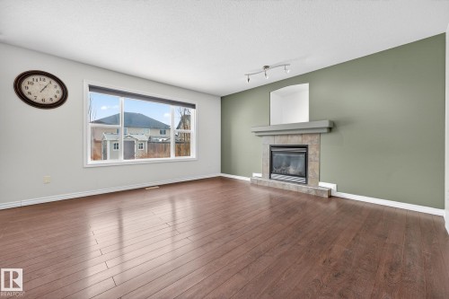 Unfurnished living room featuring dark wood-style flooring, a fireplace, track lighting, and a textured ceiling - 152 Rue Marquet, Beaumont, AB - Indoor Photo Showing Living Room With Fireplace