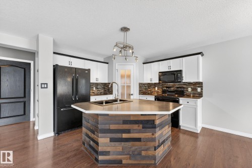 Kitchen featuring backsplash, black appliances, white cabinetry, a center island with sink, and a textured ceiling - 152 Rue Marquet, Beaumont, AB - Indoor Photo Showing Kitchen With Double Sink