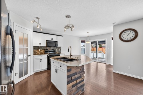 Kitchen with black appliances, tasteful backsplash, white cabinetry, a center island with sink, and a textured ceiling - 152 Rue Marquet, Beaumont, AB - Indoor Photo Showing Kitchen With Double Sink