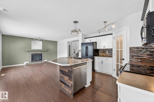 Kitchen featuring open floor plan, white cabinetry, rail lighting, a center island with sink, and black appliances - 152 Rue Marquet, Beaumont, AB - Indoor With Fireplace
