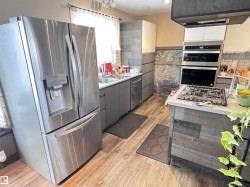 Dual tone kitchen featuring dual tone cabinets, stainless steel appliances, light countertops, light wood finished floors, and extractor fan - 