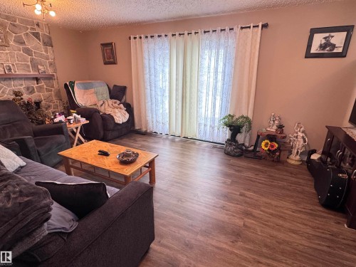 Living area with a textured ceiling, a stone fireplace, and wood finished floors - 10503 110 Street, Westlock, AB 