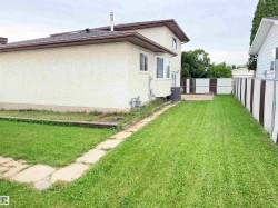 Expansive side yard featuring a manicured lawn, concrete paver pathway, and chain-link fencing - 