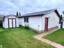 Exterior building featuring textured stucco siding, a shingle roof, and a side entry door - 10503 110 Street, Westlock, AB 