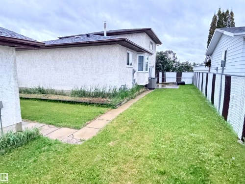 Expansive lawn area featuring a concrete patio, chain-link fencing, and a stucco exterior - 10503 110 Street, Westlock, AB 