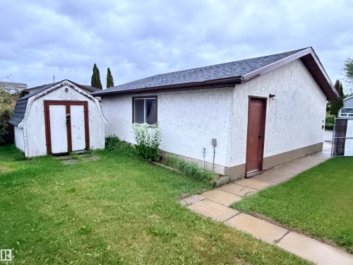 Exterior building featuring textured stucco siding, a shingle roof, and a side entry door - 10503 110 Street, Westlock, AB 