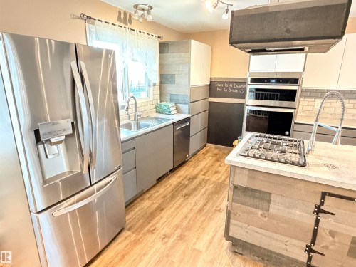 Stainless steel French door refrigerator, wood-finish flooring, undermount sink, built-in double oven, and gas cooktop - 10503 110 Street, Westlock, AB 