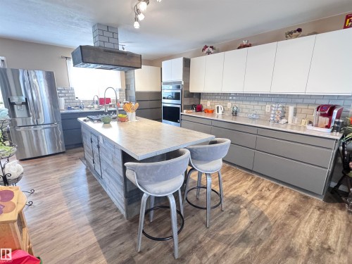 Two tone kitchen with two tone cabinets, stainless steel appliances, light countertops, decorative backsplash, and exhaust hood - 10503 110 Street, Westlock, AB 