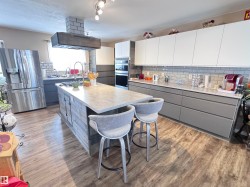Two tone kitchen with two tone cabinets, stainless steel appliances, light countertops, decorative backsplash, and exhaust hood - 