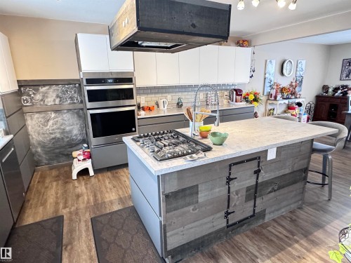 Dual tone kitchen with light countertops, exhaust hood, decorative backsplash, stainless steel appliances, and modern cabinets - 10503 110 Street, Westlock, AB 