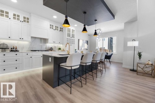 Dual tone kitchen featuring a breakfast bar, hanging light fixtures, a kitchen island with sink, light stone countertops, and two tone cabinets - 3722 41 Avenue, Beaumont, AB - Indoor Photo Showing Kitchen With Upgraded Kitchen